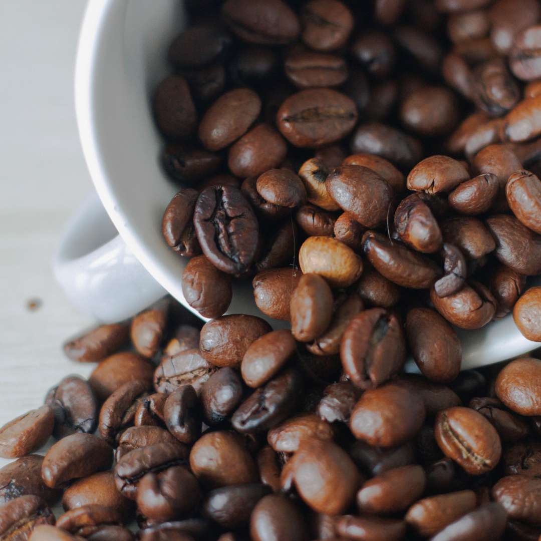 Close-up of roasted coffee beans spilling from a white cup representing premium Turkish coffee online
