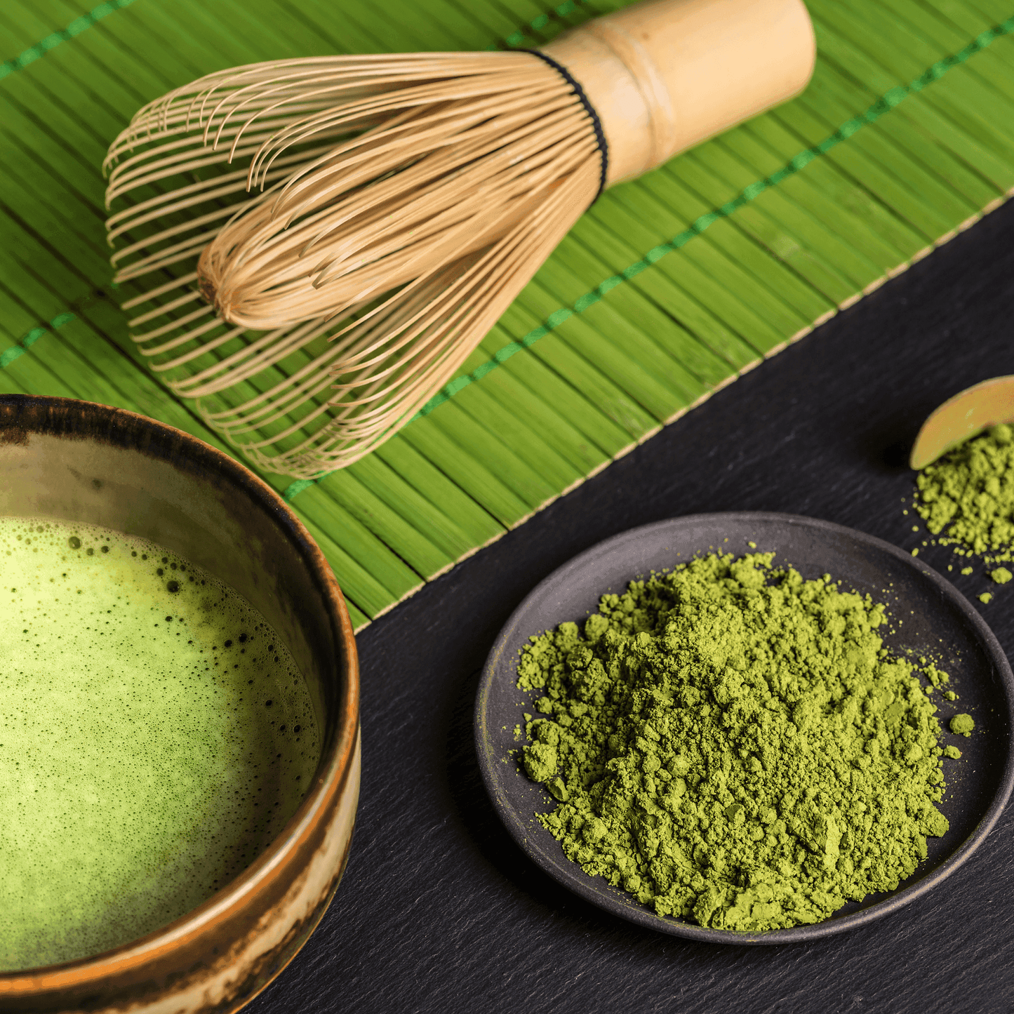 Cup of creamy matcha latte with premium matcha latte powder and whisk on bamboo mat