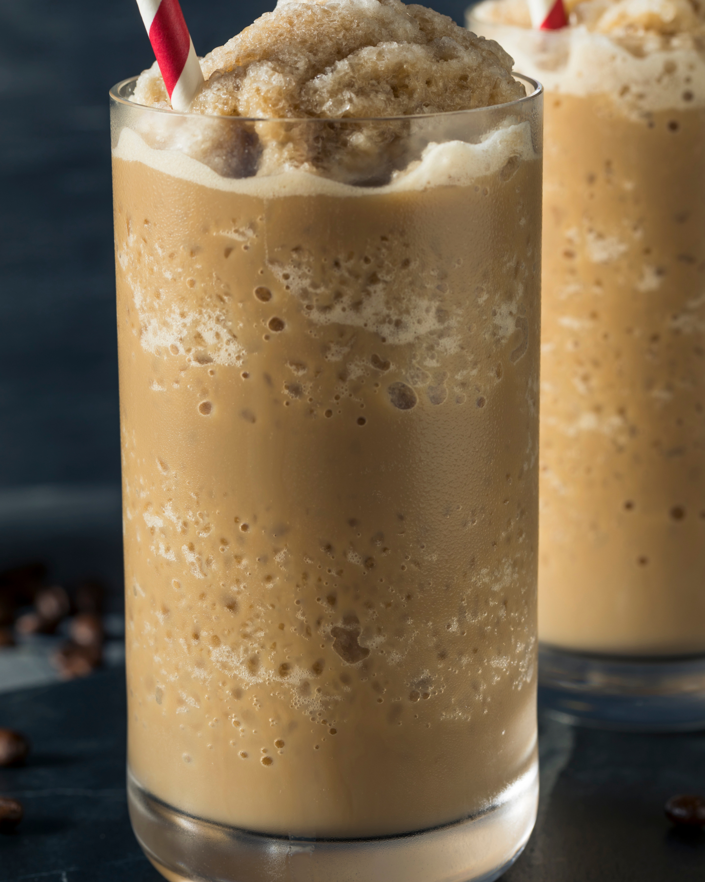 Glass of iced coffee made with premium coffee powder by Caffeeegy.Co with frothy top and red striped straw