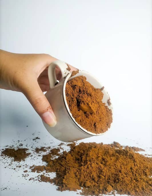 Hand holding white cup filled with freshly roasted Turkish coffee beans ground in powder form by Caffeeegy Co