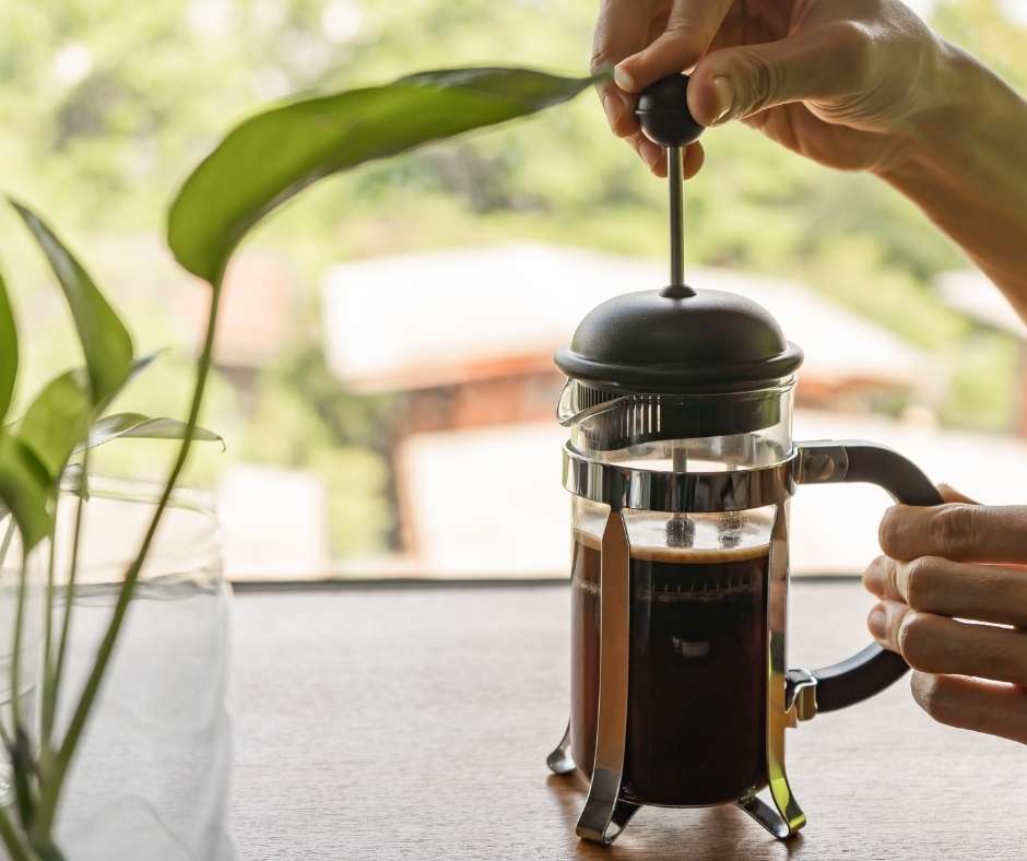 Person using a French press to brew freshly roasted American coffee at a sunny window