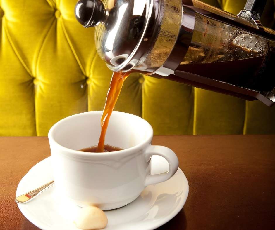 Freshly roasted American coffee being poured from a French press into a white cup