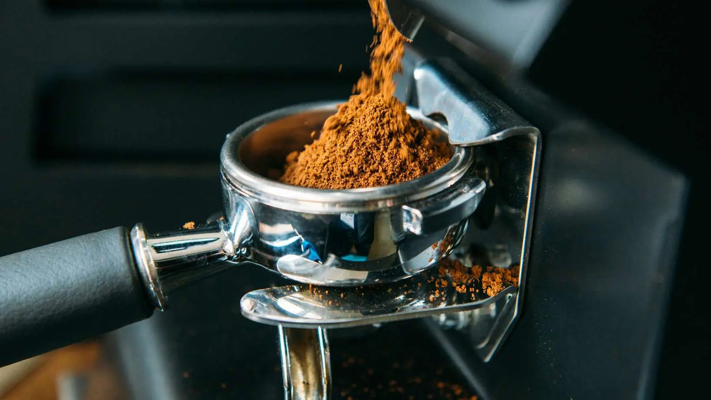 Ground premium espresso coffee blend being poured into a portafilter for espresso machine