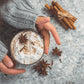 Cozy hand holding a cup of spice chai latte powder topped with whipped cream and spices