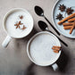 Two cups of creamy spice chai latte powder topped with cinnamon and star anise on a textured surface